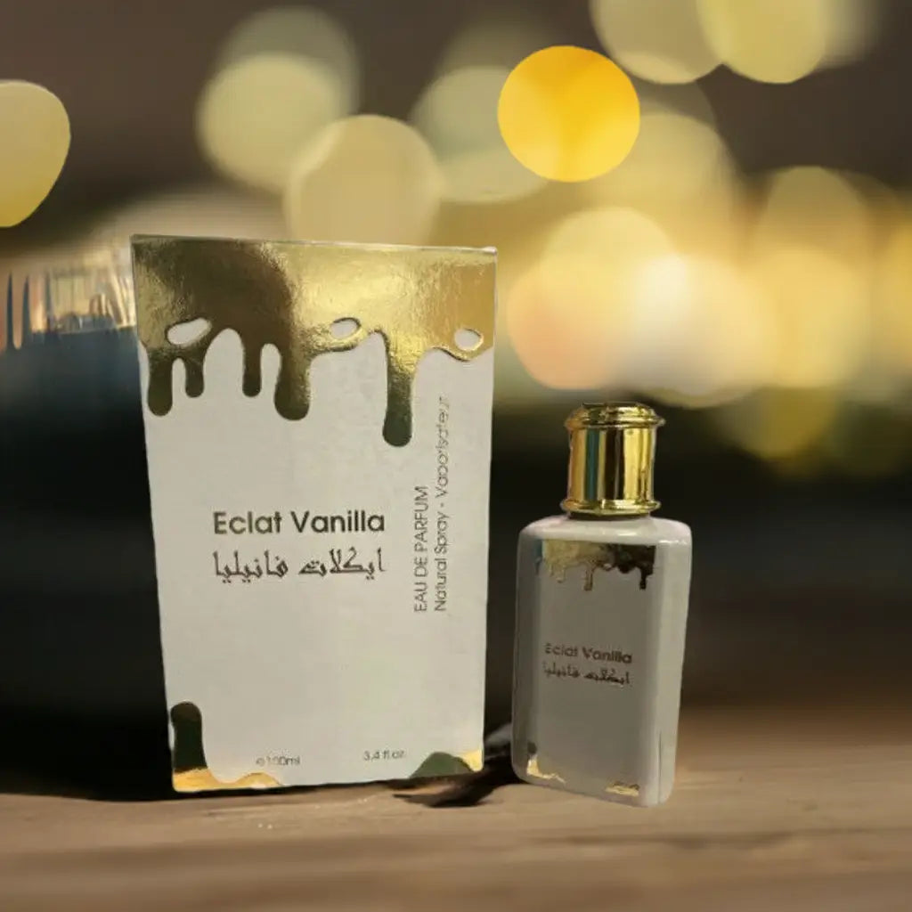 Witte rechthoekige parfumfles met gouden accenten en druppelend gouden ontwerp naast bijpassende doos van eclat vanilla for her door fc